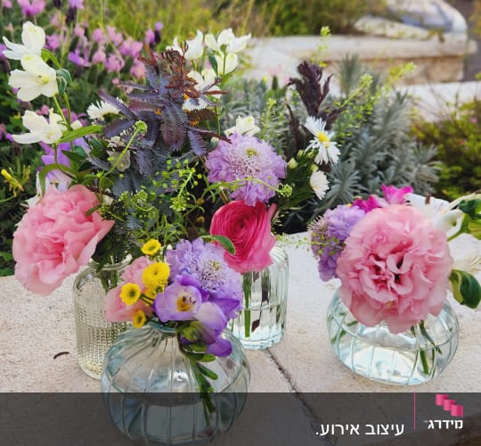 שלושה אגרטלים עם פרחים צבעוניים על שולחן אבן